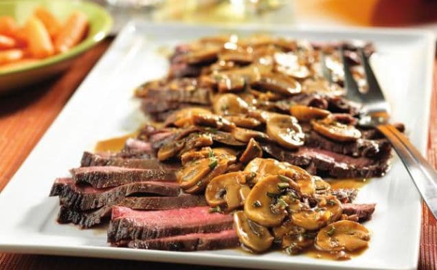 Sliced flank steak on a platter topped with mushroom sauce