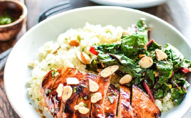 Bowl of sliced barbecue chicken over cauliflower couscous with greens and almonds